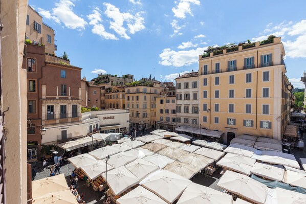 Une zone de marché en plein air animée, avec de nombreux parasols blancs, entourée d’immeubles à plusieurs étages dotés de balcons et de commerces.