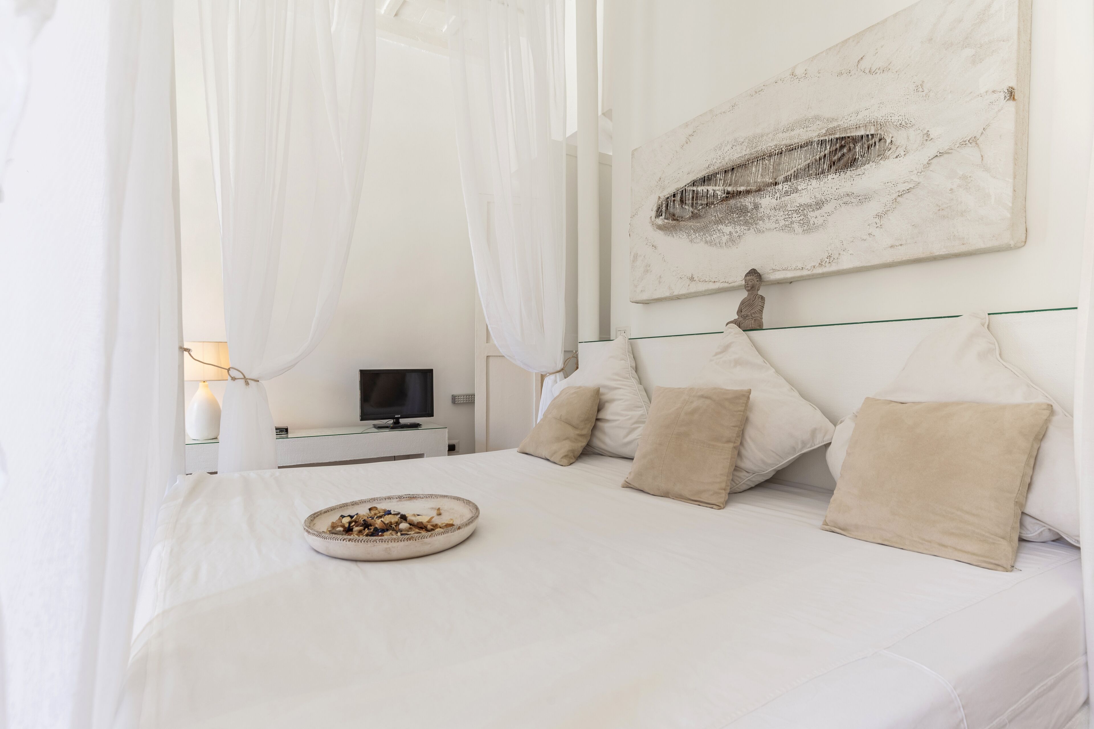 A bedroom with a bed, a television, and a painting on the wall.