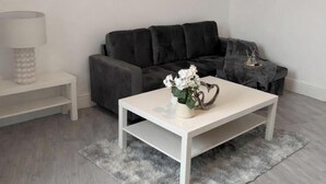 Un salon moderne avec une table basse blanche, un canapé gris et un tableau représentant un paysage urbain accroché au mur.