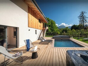 A modern outdoor pool area with lounge chairs, a hot tub, and a wooden deck.
