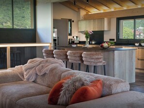 A modern kitchen with a central island, bar stools, and a view of the outdoors. - Chalet Tyron - The Alps at all season in a rural setting - OVO Network (Val de Chaise)