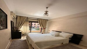Ein Schlafzimmer mit einem großen Bett, einem Fernseher, einer Kommode und einem Fenster mit Vorhängen.