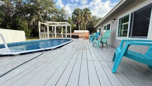 Eine Holzterrasse mit Pool, Gartenmöbeln und einem überdachten Bereich.