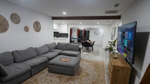 Una sala moderna con un sofá seccional gris, un mueble bajo para la televisión de madera y una alfombra estampada.