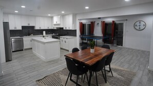 Cocina moderna con armarios blancos, una isla central y una zona de comedor con mesa y sillas de madera.