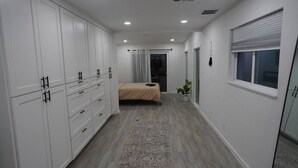 Un dormitorio con cama, mesita de noche, planta en maceta y ventana con persianas.