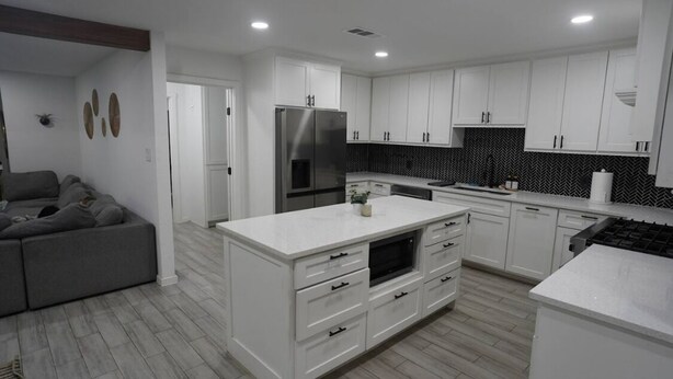 Una cocina moderna con armarios blancos, horno integrado y un sofá gris en la sala.