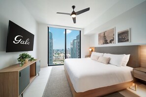 Ein modernes Hotelzimmer mit einem großen Bett, einem Deckenventilator, einem Fernseher, Blick auf die Stadt und Kunstwerken an den Wänden.