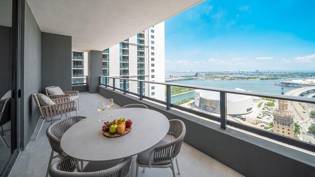Ein Balkon mit rundem Tisch, Korbstühlen und einer Obstschale mit Weingläsern.