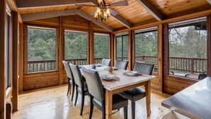 A wooden dining room with a large table and chairs, large windows, and a ceiling fan.