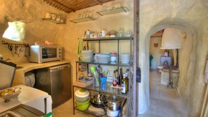 A rustic kitchen with a microwave, sink, and shelves holding dishes and utensils. - Proven al Bergerie With Pool Sleeps 4 Gordes (Gordes)