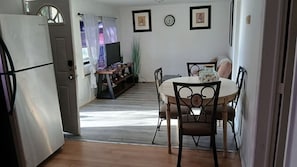Una cocina compacta con refrigerador, una mesa de comedor con sillas, un reloj y una ventana con cortinas.
