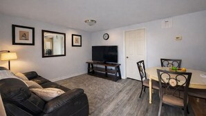 Een woonkamer met een bank, tv-meubel en een eettafel met stoelen.