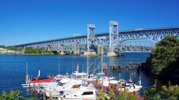 A marina with boats docked, a bridge in the background, and clear blue skies.