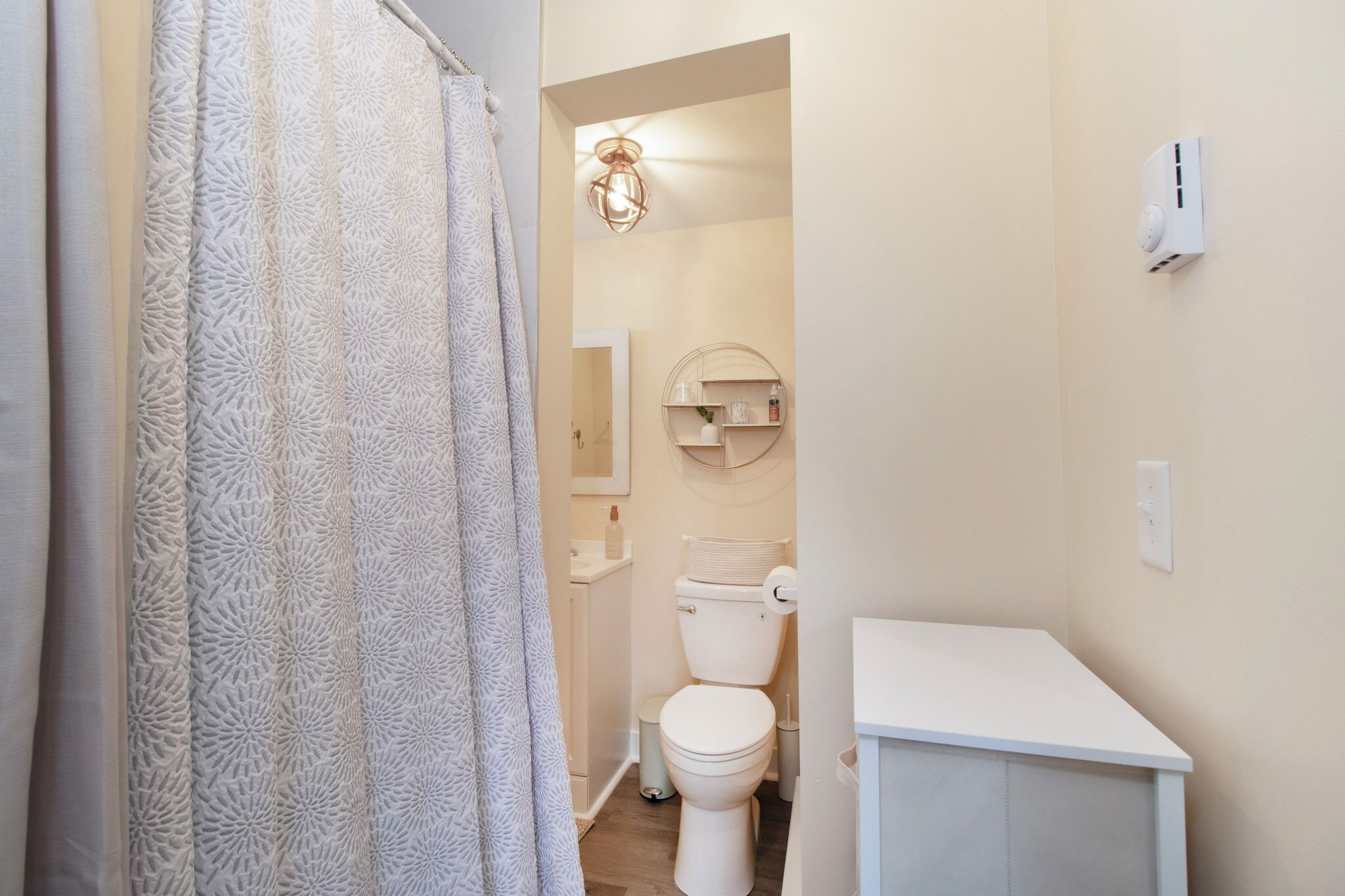 Une salle de bain avec des toilettes, une petite étagère contenant des articles de toilette et un rideau de douche.