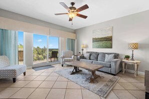 A spacious living room with a ceiling fan, a sofa, a coffee table, and a view through large sliding glass doors. - Exclusive 2BR Condo with Beach Access (Miramar Beach)