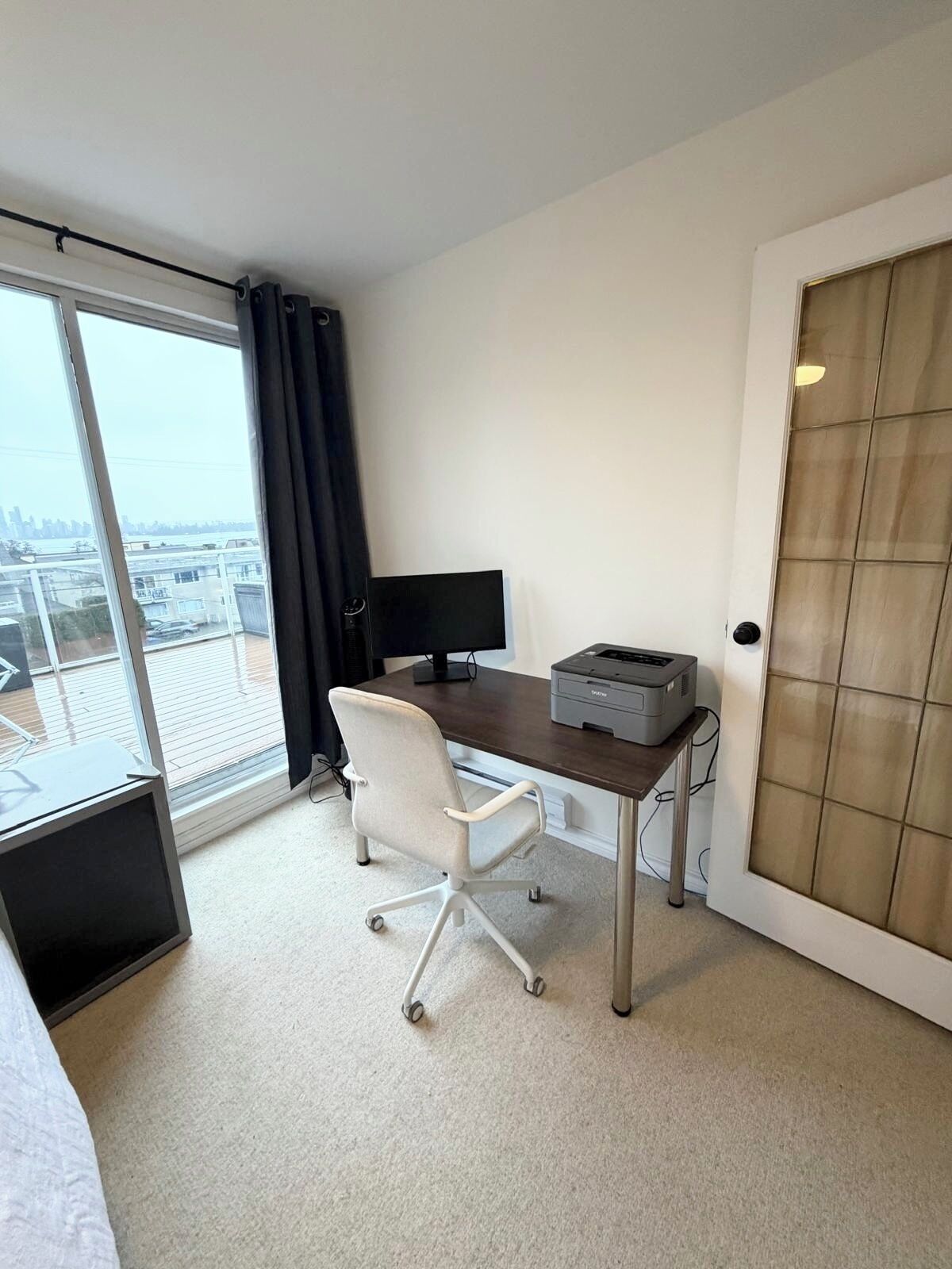 A small, modern hotel room with a desk, chair, and a large window offering a city view.