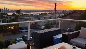 Un balcone con un elemento decorativo a fuoco, posti a sedere all'aperto e vista sullo skyline cittadino al tramonto.