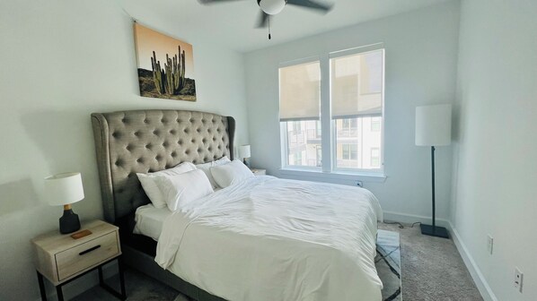 A bedroom with a tufted headboard, a large window, a bedside table with a lamp, and a painting on the wall. - Modern Clean 1/1 Near Downtown Gym Pool (Austin)