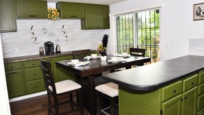 Cozinha com armários verdes, ilha de madeira escura e janela com vista para o verde.