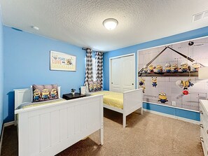 Une chambre avec un lit superposé, un bureau et un mur décoré de personnages de « Moi, moche et méchant ».