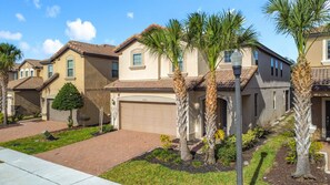 A residential neighborhood with single-family homes, a paved driveway, and well-maintained landscaping including palm trees and shrubs. - Solterra Peaceful 6BR Villa, Private Pool, GameRm (Davenport)