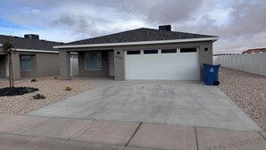 A modern two-story house with a garage, driveway, and a blue recycling bin.