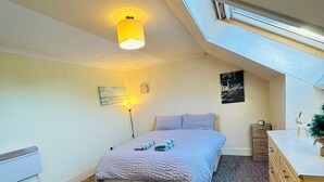 Une chambre à coucher avec un lit, une commode, une lampe et une lucarne.