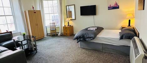 Une chambre d’hôtel comprenant un lit, un bureau, une chaise, une armoire, une télévision et une fenêtre.