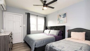 Ein Schlafzimmer mit zwei Betten, einem Deckenventilator, einem Fenster mit Vorhängen und einer Tür.