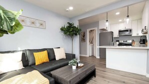 Ein modernes Wohnzimmer mit einem schwarzen Ledersofa, einem Holztisch und einer Küchenzeile mit weißen Schränken und Edelstahlgeräten.
