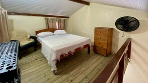 A bedroom with a wooden floor, a bed with a white bedspread, a wooden dresser, and a ceiling fan. - Pousada Estação Ferrugem (Garopaba)