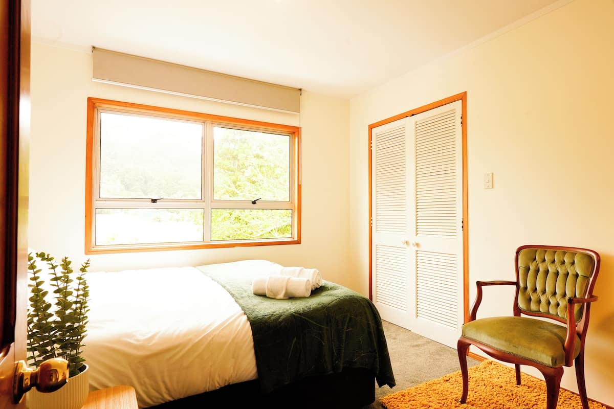 Une chambre à coucher avec un lit, une fenêtre, un fauteuil vert et une plante.