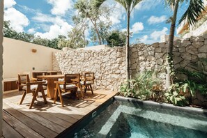 An outdoor patio with a stone wall, wooden deck, and a pool. - Luxe Villa 10p, Grill, 2 Private Pools w/Concierge (Tulum)