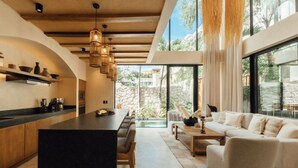 A modern kitchen with a central island, bar seating, and a dining area with a sofa and coffee table. - Luxe Villa 10p, Grill, 2 Private Pools w/Concierge (Tulum)