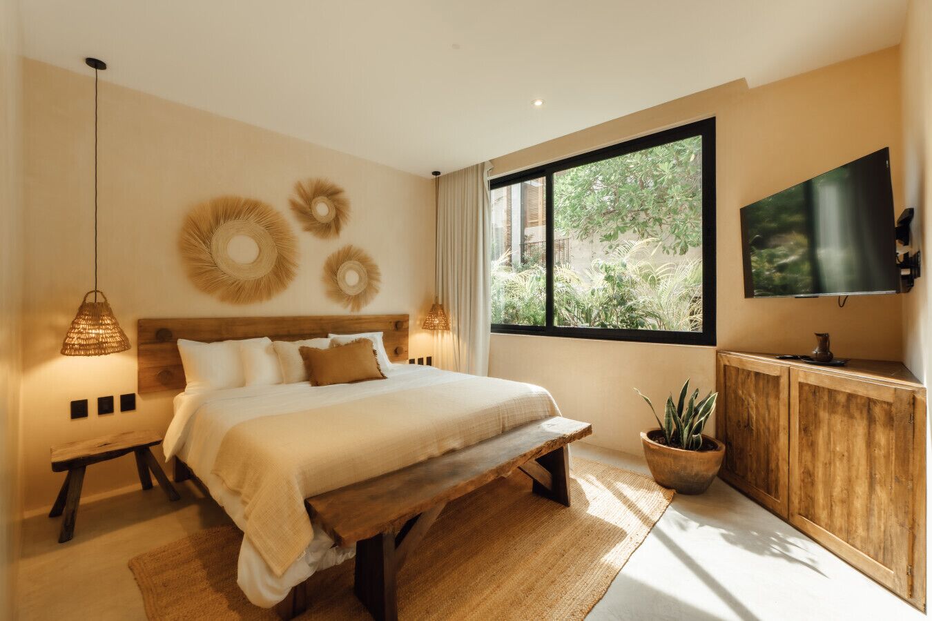 Une chambre dotée d’un grand lit, d’une tête de lit en bois, d’un téléviseur fixé au mur et d’une fenêtre donnant sur un paysage verdoyant.