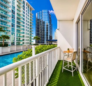 A balcony with a pool, white railing, and a table with chairs. - Brickell Studio: Free Parking, Pool & Private Patio (Miami)
