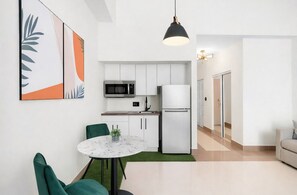 A modern kitchen with white cabinets, a microwave, and a refrigerator. There is a dining area with a round table and green chairs. - Brickell Studio: Free Parking, Pool & Private Patio (Miami)