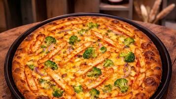 A pizza with broccoli and chicken on a round black tray.