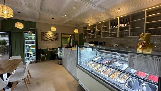 L’intérieur d’un restaurant avec un présentoir central de glaces, un plafond en bois et des murs verts.