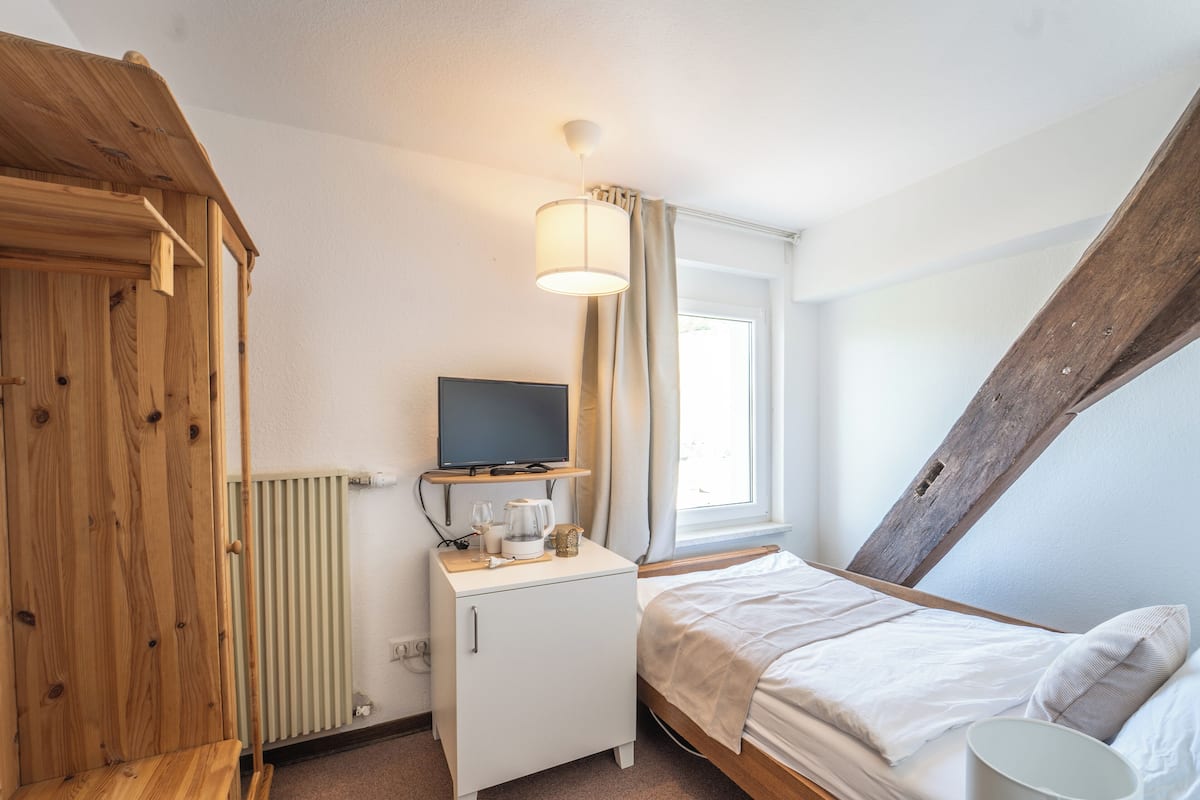 Une chambre à coucher avec un lit, un bureau avec une télévision, un radiateur et une fenêtre avec des rideaux.