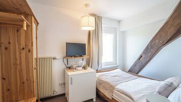 Ein Schlafzimmer mit einem Bett, einem Schreibtisch mit Fernseher, einem Heizkörper und einem Fenster mit Vorhängen.