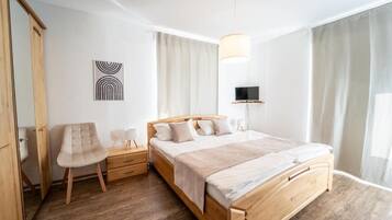 A modern bedroom with a wooden bed, a bedside table, a chair, a TV mounted on the wall, and a window with curtains.
