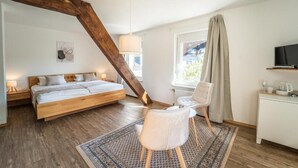 Une chambre à coucher avec un lit en bois, une chaise, un bureau avec une télévision et une fenêtre avec des rideaux.