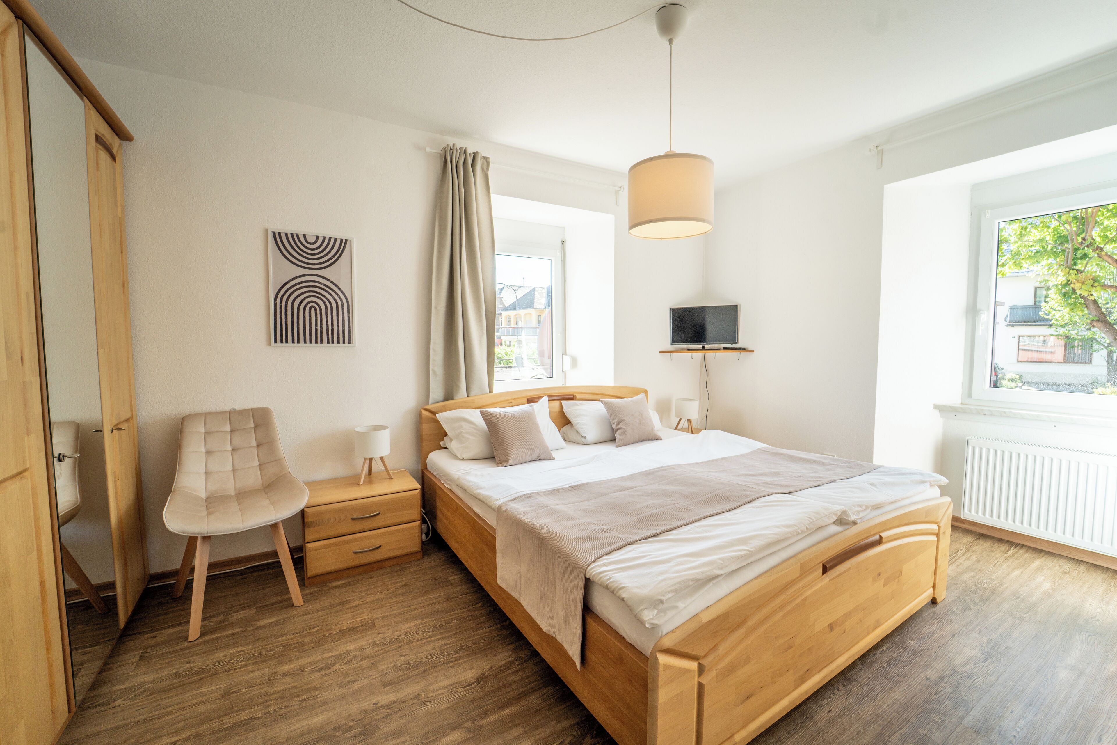 Ein Schlafzimmer mit einem hölzernen Bett, einem Sessel, einem Nachttisch, einer Lampe und einem Fernseher.