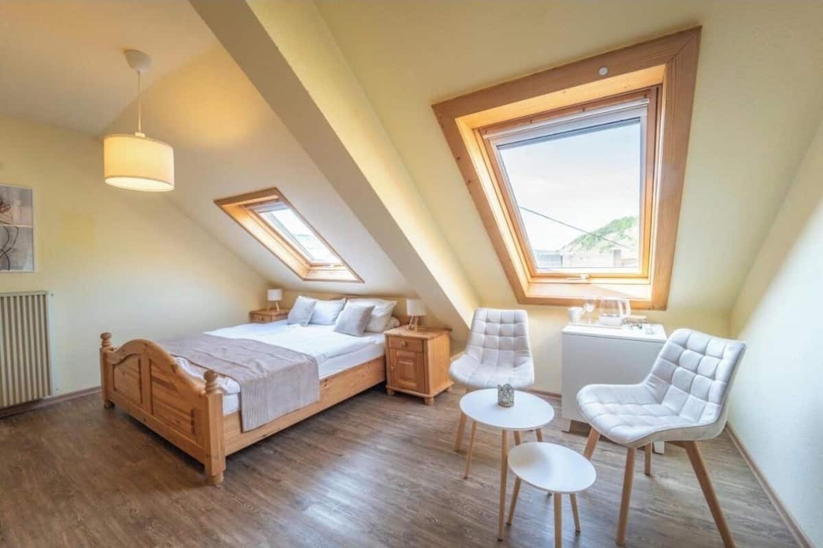 Une chambre à coucher avec un lit en bois, deux tables de chevet, une chaise, une petite table et une fenêtre donnant sur un beau paysage.