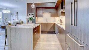 A modern kitchen with a marble island, wooden cabinets, and stainless steel appliances. - Skyline Penthouse - CN Tower Downtown (Toronto)