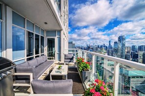 Terraza en la azotea con sofá, mesa y parrilla, con vistas a un horizonte urbano.