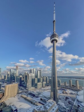 A high-rise tower with a distinctive observation deck, surrounded by modern skyscrapers and a body of water in the background. - Skyline Penthouse - CN Tower Downtown (Toronto)