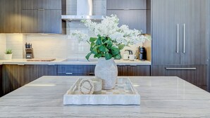 A modern kitchen with dark wood cabinets, a marble countertop, and a vase with white flowers. - Skyline Penthouse - CN Tower Downtown (Toronto)